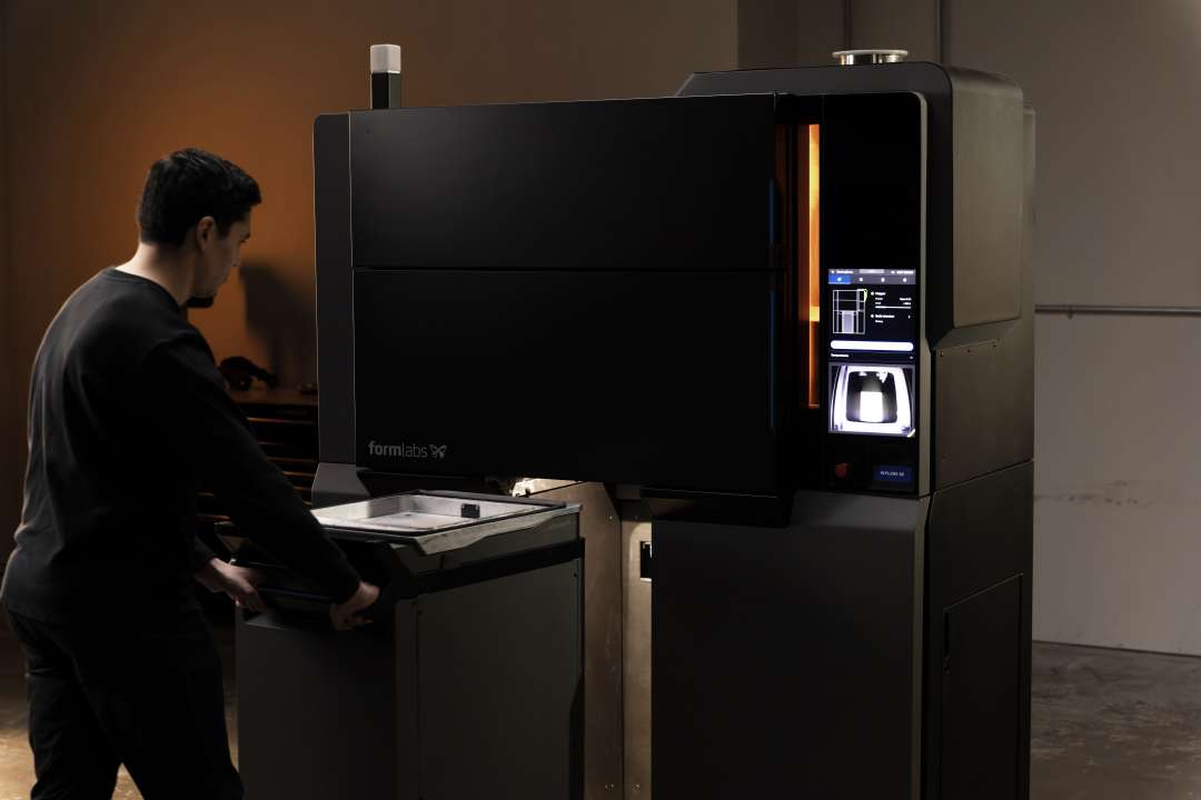 Mitarbeiter mit geöffnetem Deckel der Formlabs Fuse X1 Build Unit neben dem aktiven Fuse X1 SLS-Drucker beim Zugriff auf den Kammerinhalt nach Druckabschluss