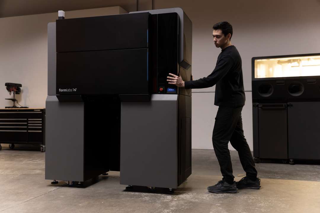 Formlabs Fuse X1 SLS printer being repositioned on its wheeled transport base; Fuse Sift X1 breakout station visible in the background
