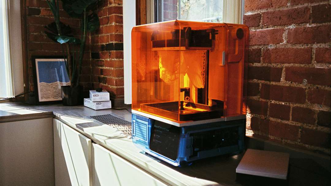 Formlabs Form Studio 1 Basic Graphite — SLA 3D-Drucker auf einem Schreibtisch mit einer orangefarbenen Schutzabdeckung